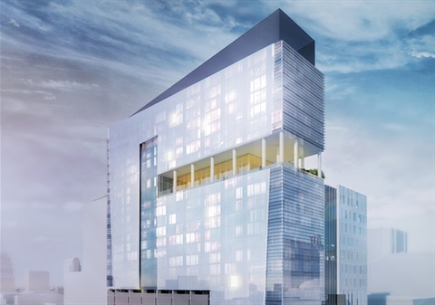 A tall, modern glass building with sharp angular lines rises against a cloudy sky. The structure features reflective blue‑tinted windows and a distinctive cut‑out section near the upper floors that reveals an open terrace area